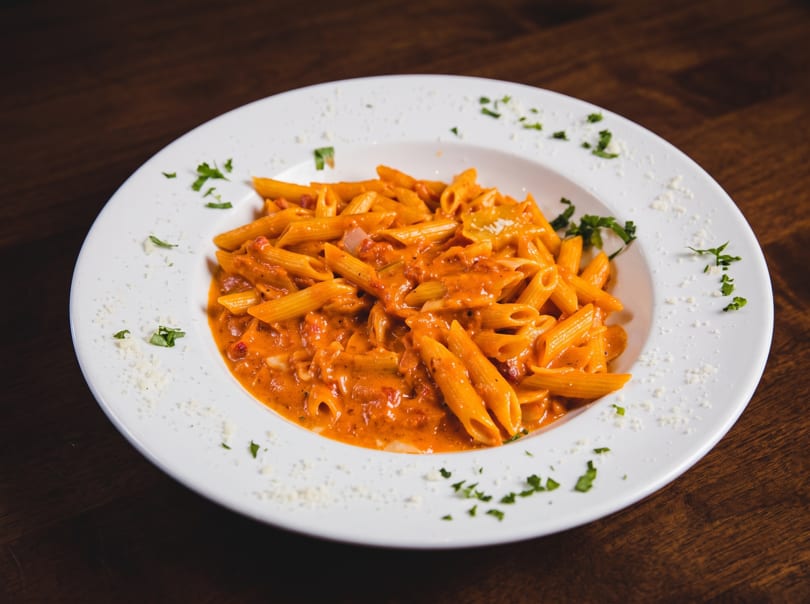 Penne pasta in creamy tomato sauce, garnished with parsley and grated cheese on a white plate.