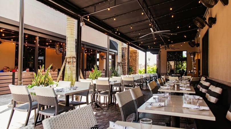 Spacious outdoor patio dining area with tables, chairs, string lights, and a long cushioned bench.