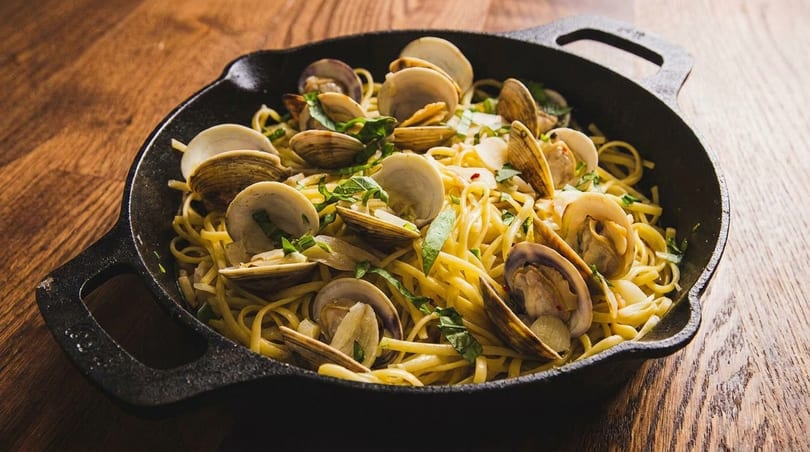 Linguine with clams, garlic, and fresh herbs in a black cast iron skillet on a wooden table.