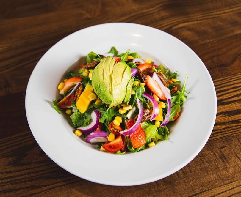 Colorful salad with avocado, strawberries, corn, red onion, and pecans in a white bowl.
